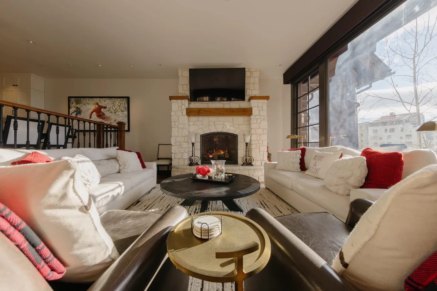 A bright living room with sofas arranged around a coffee table and stone fireplace.