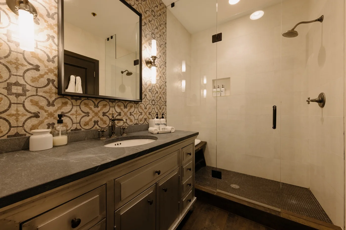Un tocador de baño con un espejo grande está junto a una ducha.