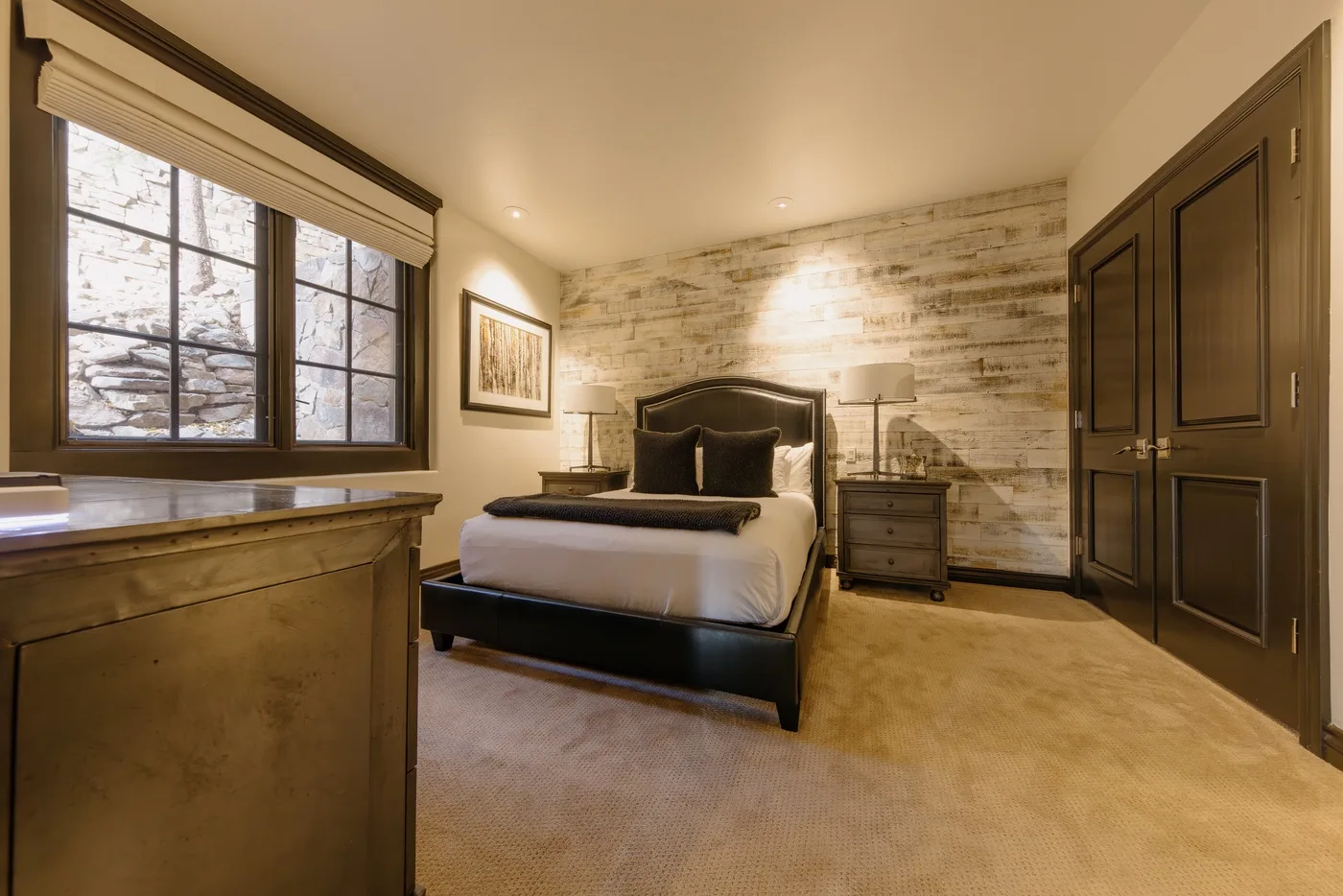 Un dormitorio con una cama, mesitas de noche y una ventana grande.