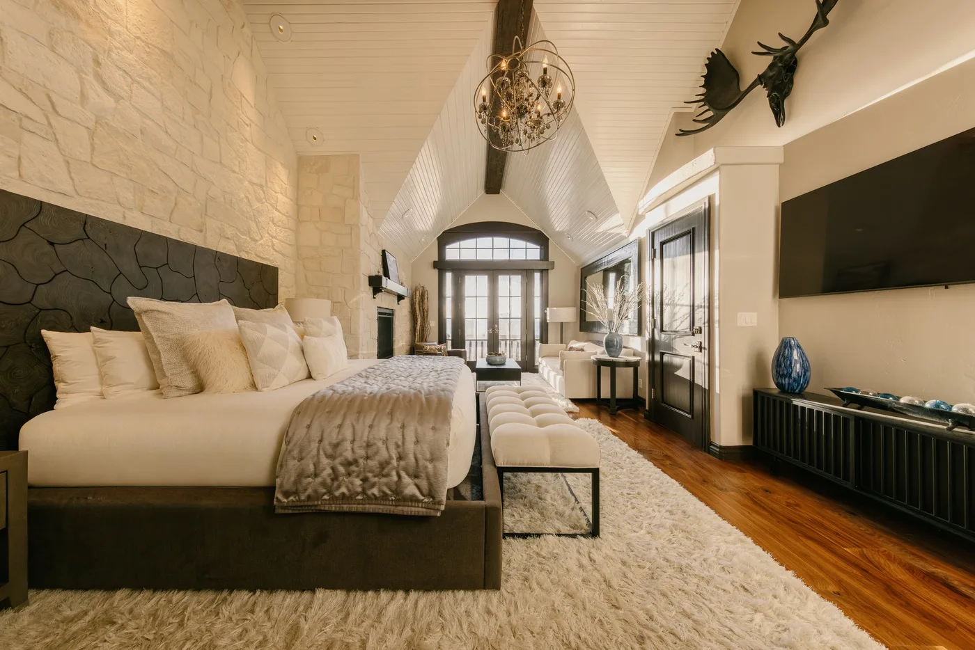 Un dormitorio amplio con una cama grande, un banco tapizado y ventanas altas.