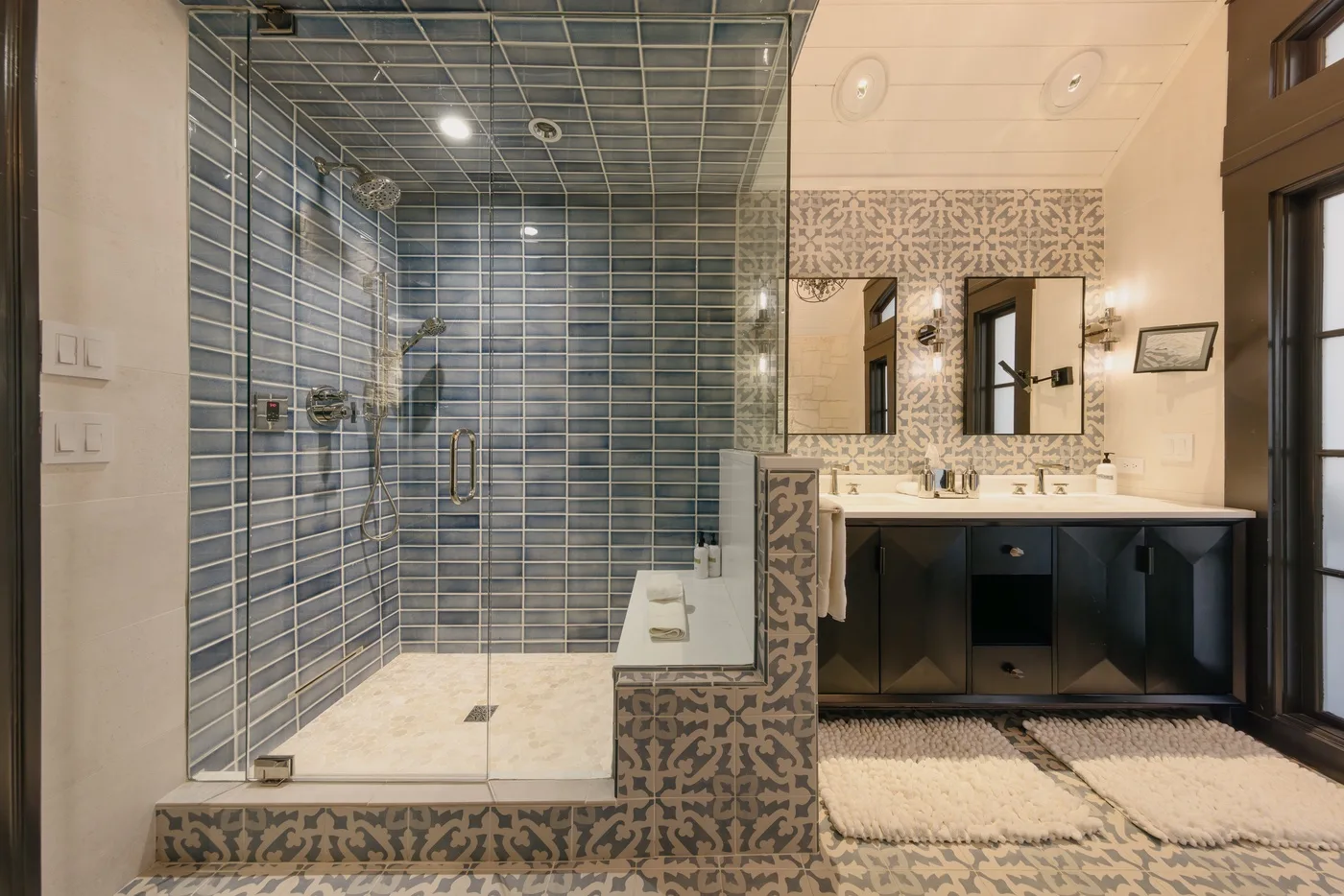 Un baño con ducha de vidrio, lavabo doble y azulejos estampados.