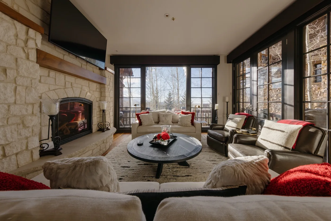A bright living room with large windows and a stone fireplace.