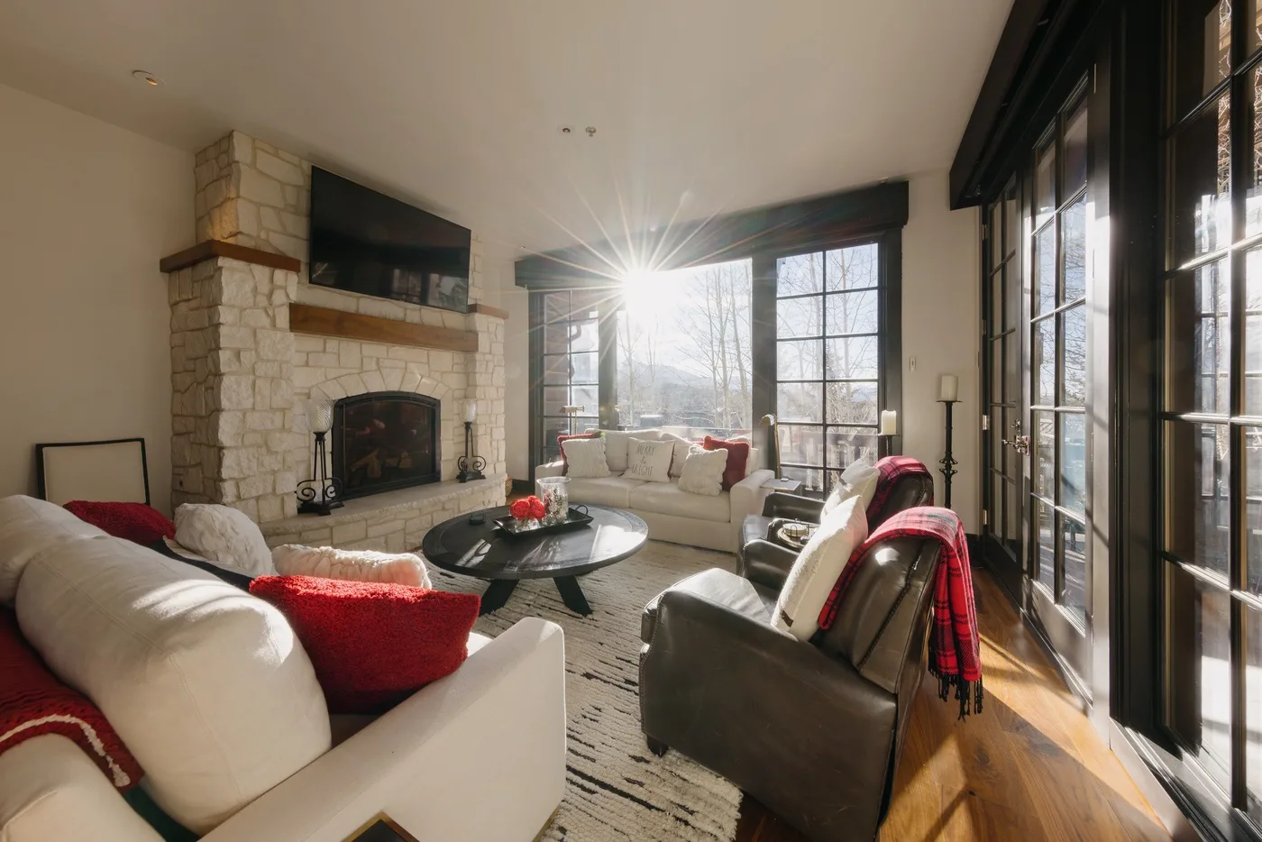 A sunlit living room with seating around a coffee table and a stone fireplace.
