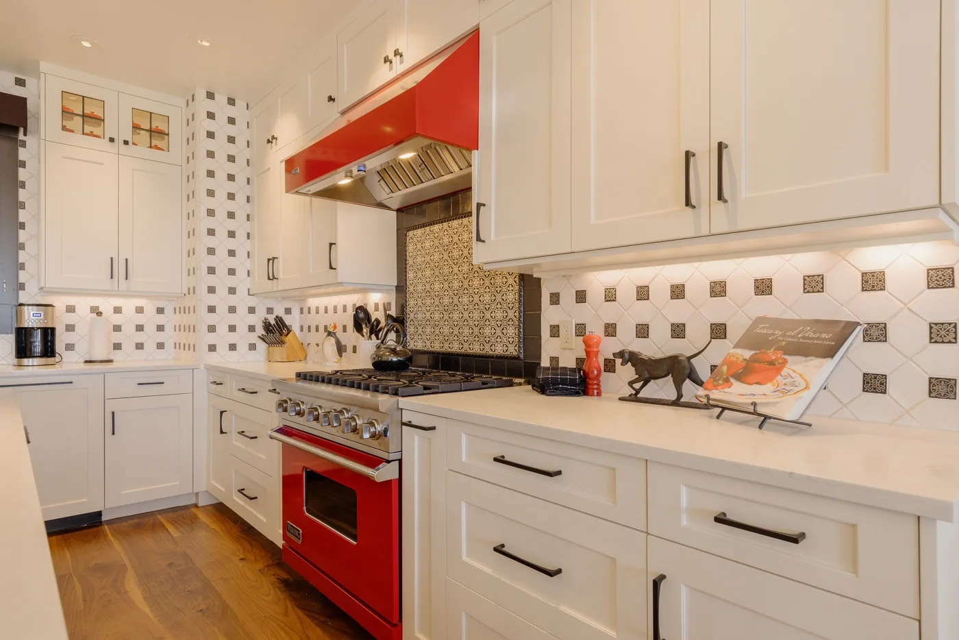 Una cocina luminosa con gabinetes blancos, azulejos estampados y una estufa roja.