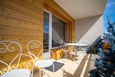 A sunny balcony with outdoor seating beside a wood-paneled wall.