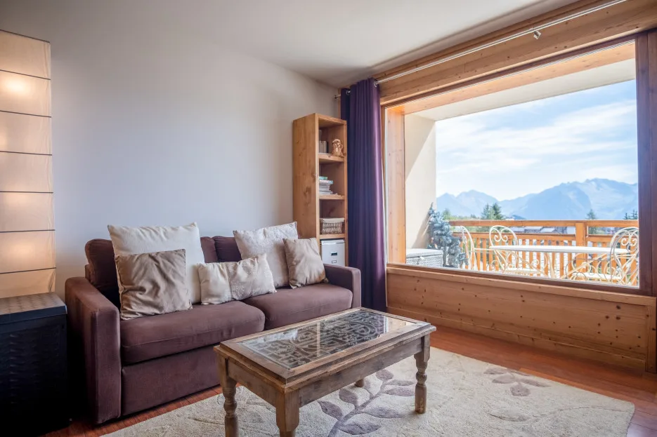 A living room with cushioned seating beside a large window overlooking mountains.