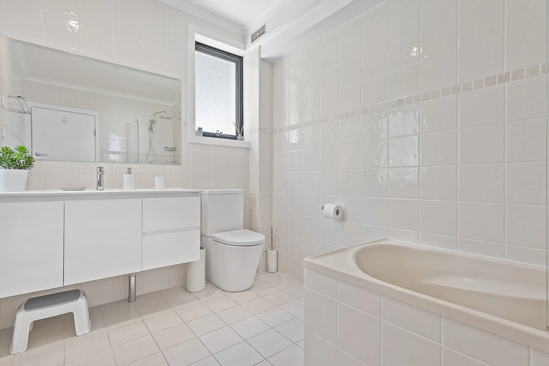 A bright bathroom with a bathtub, vanity, and window.