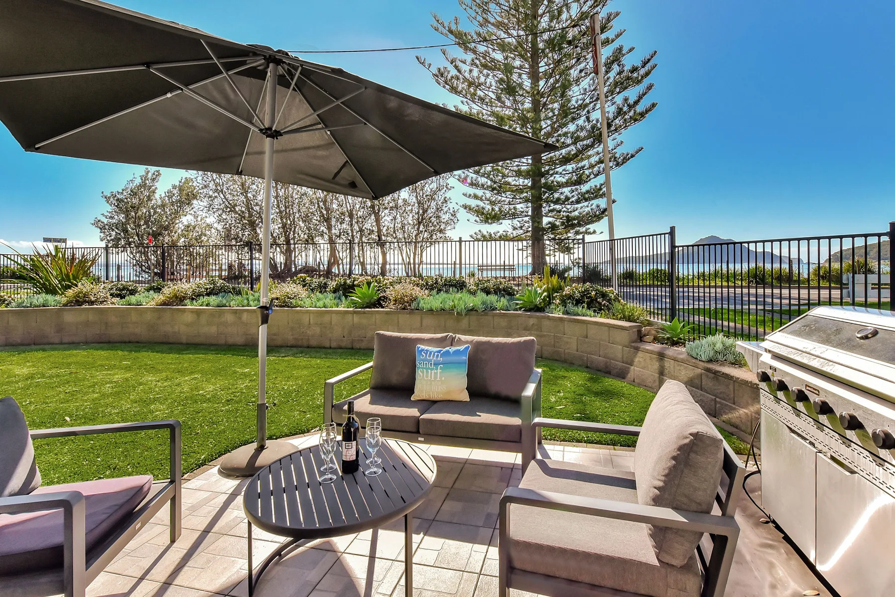 An outdoor patio with cushioned seating, a table, and an umbrella overlooks a landscaped lawn.