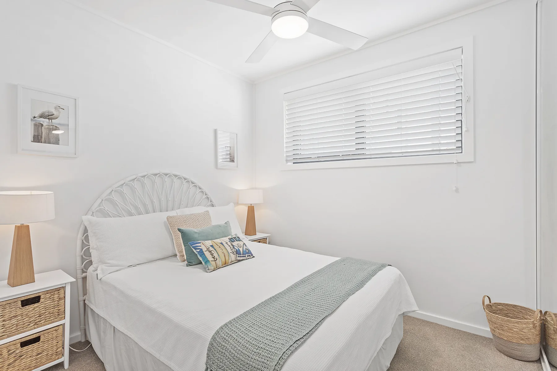 A bright bedroom with a neatly made bed and a window with closed blinds.
