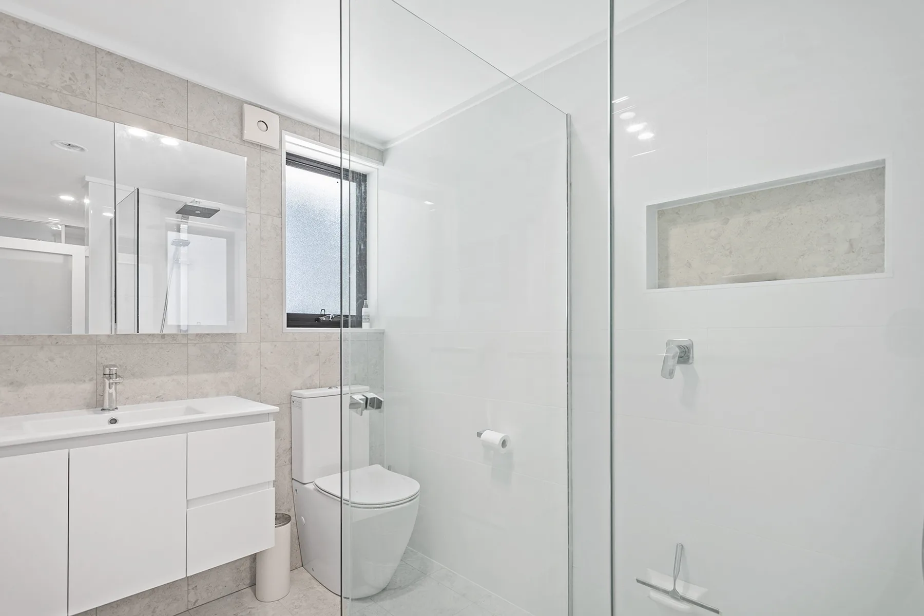 A bright bathroom with a glass shower, white vanity, and toilet.
