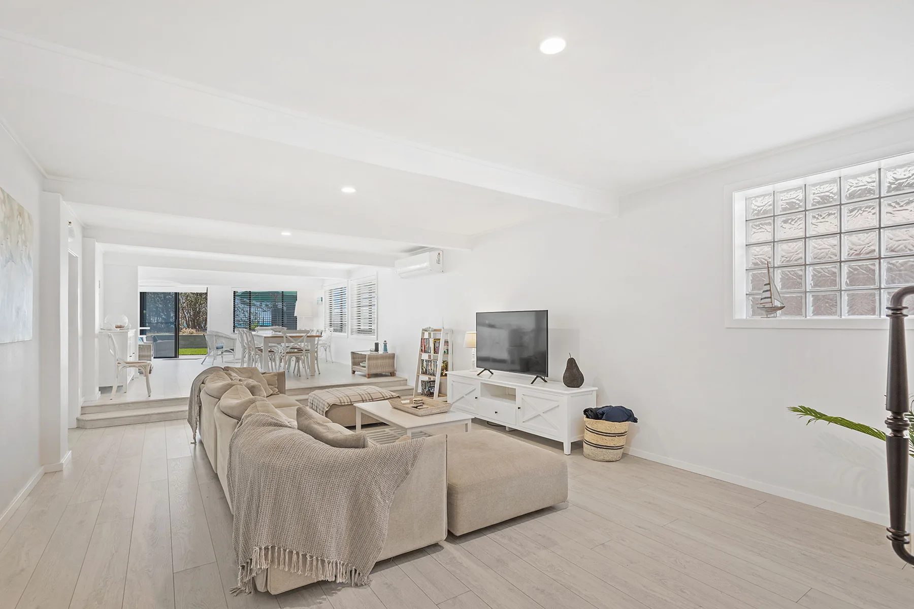 A bright living room opens into a dining area, with seating and a television.