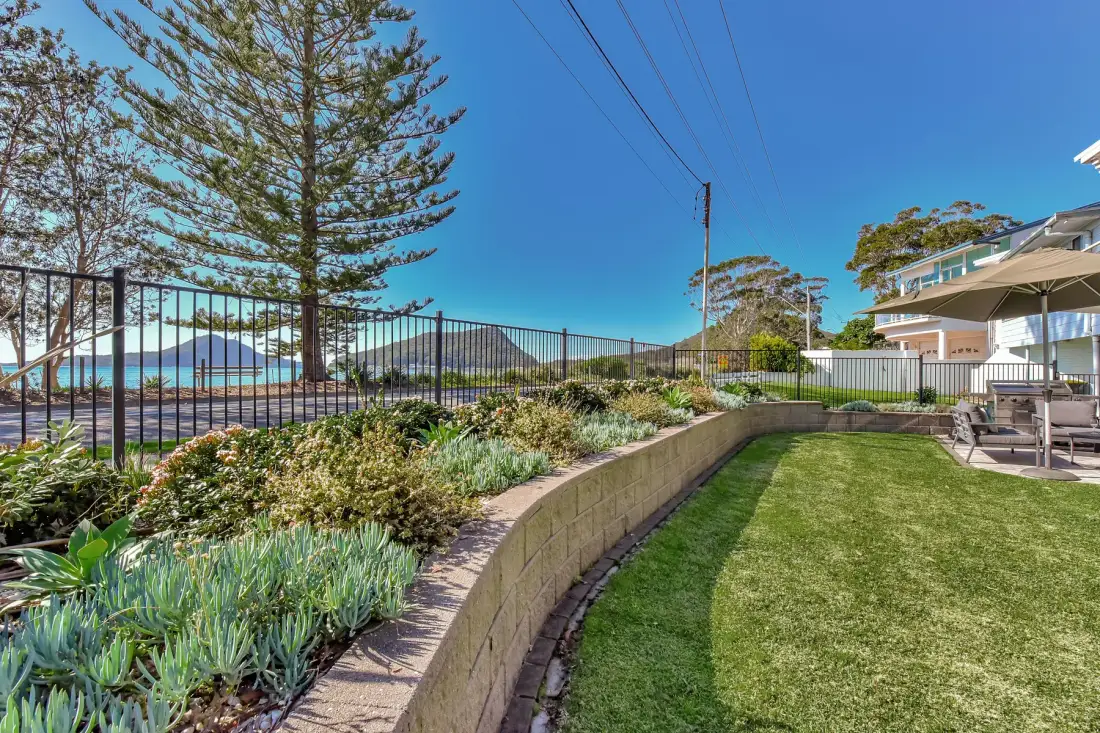 A landscaped garden and lawn overlook the water behind a metal fence.