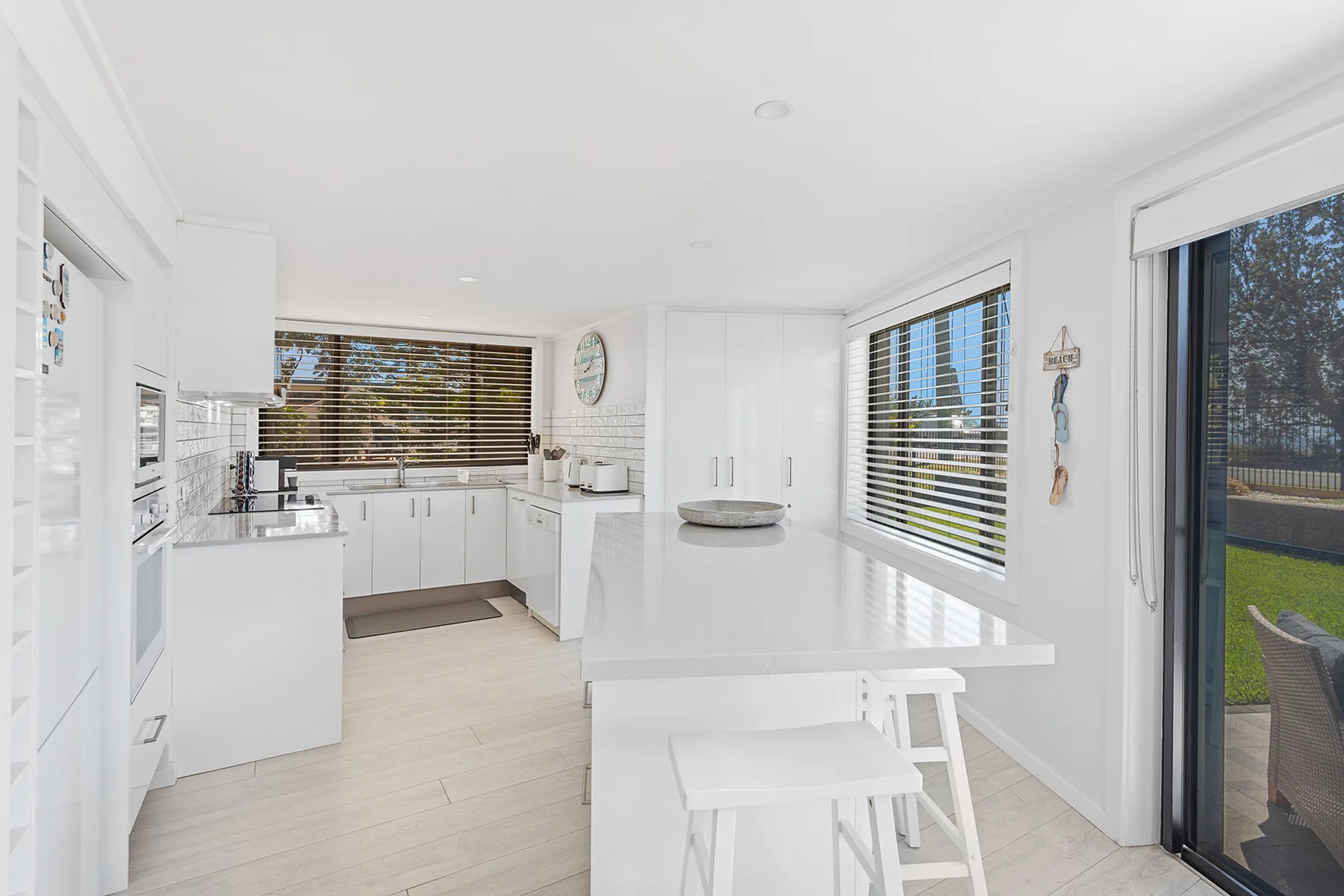 A bright kitchen with white cabinets, broad windows, and a dining counter.
