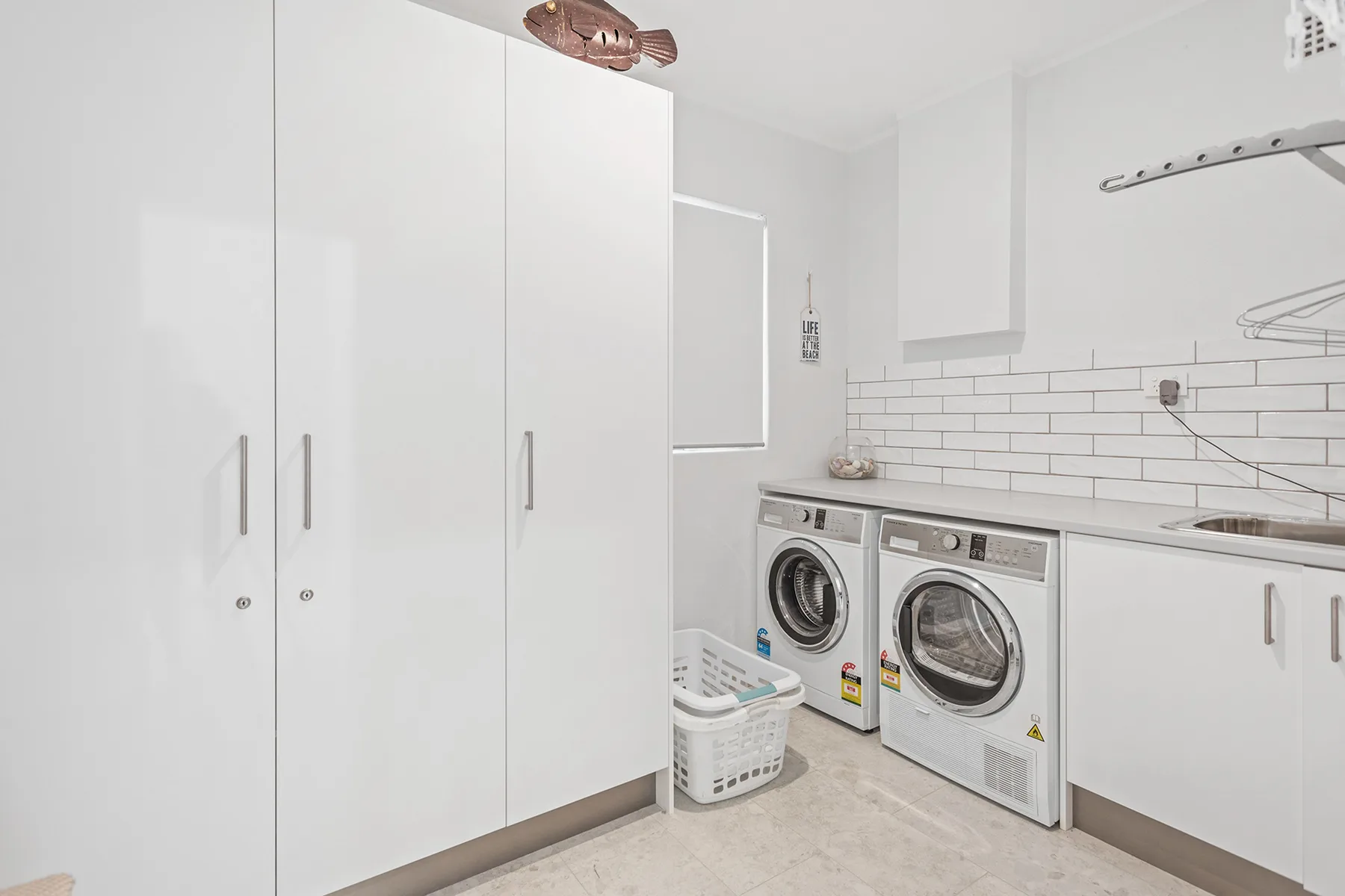 A bright laundry room with front-loading washing machines and white cabinets.