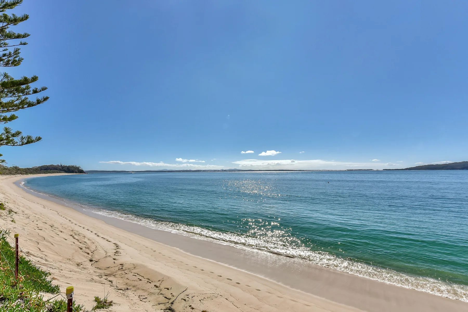A sandy beach curves along clear blue water beneath a bright sky.