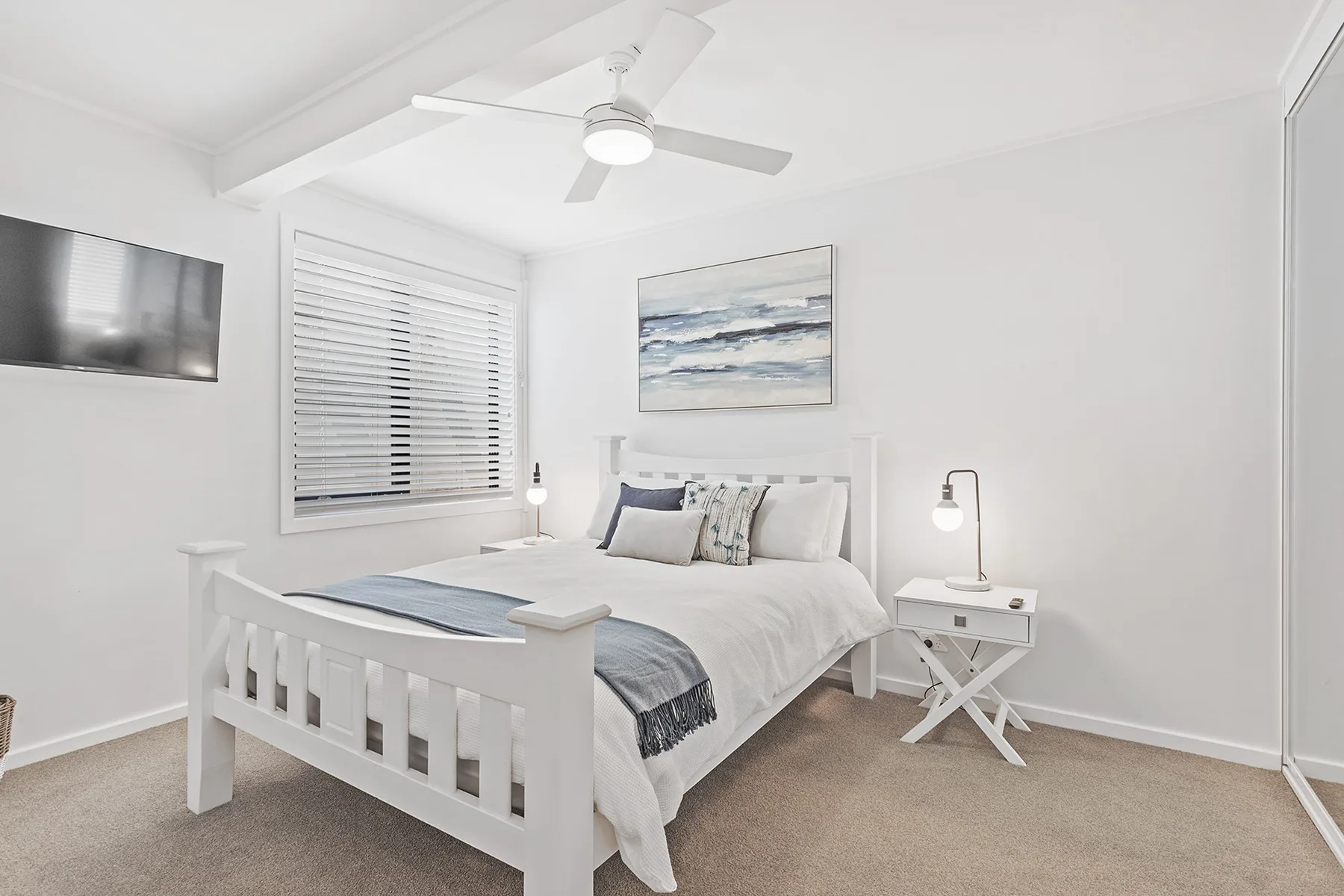 A bright bedroom with a white bed, bedside tables, and a ceiling fan.
