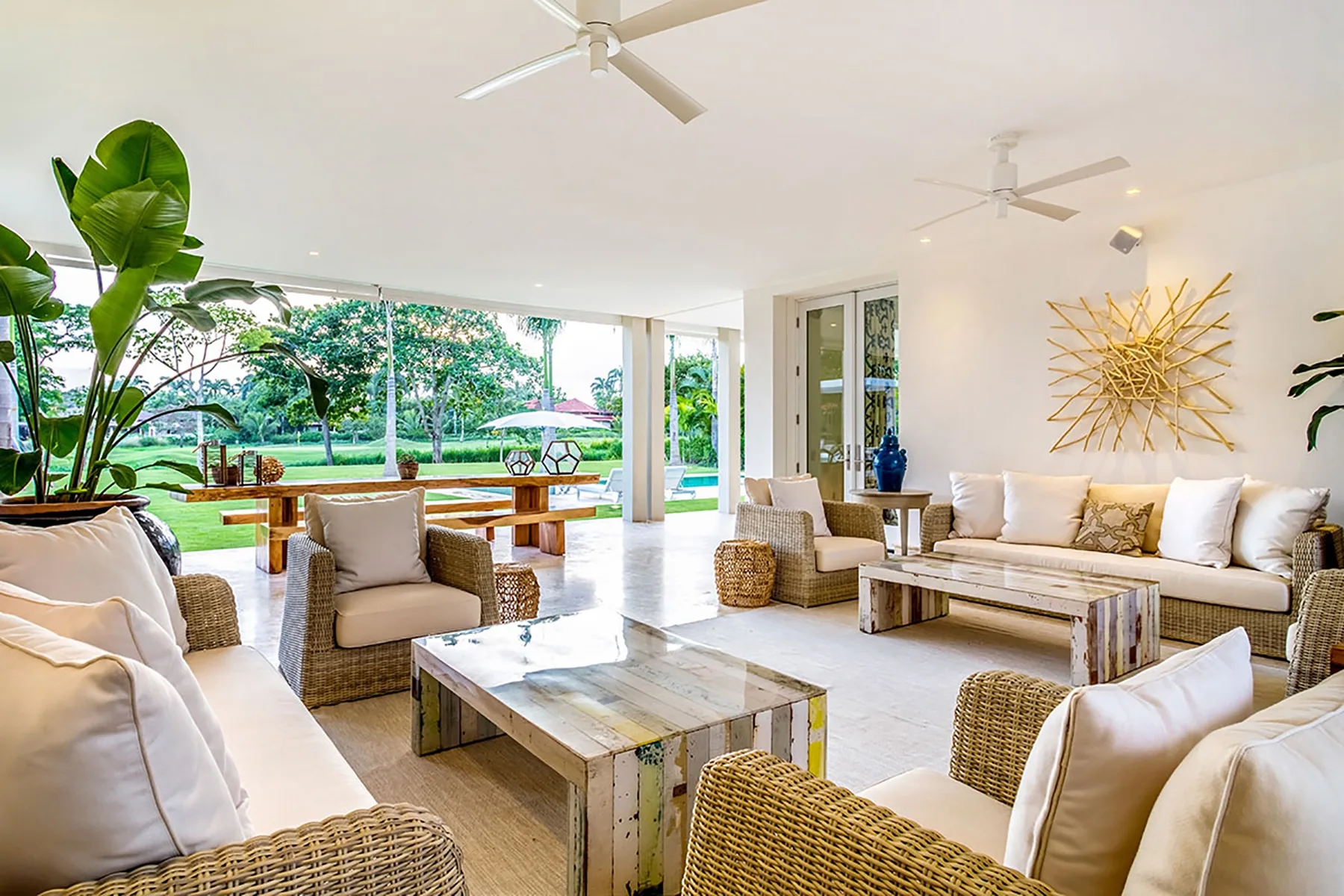 Una luminosa sala de estar se abre a un patio con jardín, con asientos tejidos y una mesa baja.