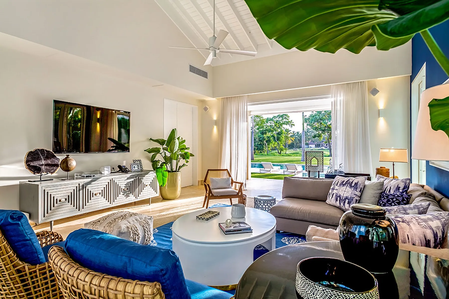 Bright living room with a television, seating, and large windows overlooking greenery.