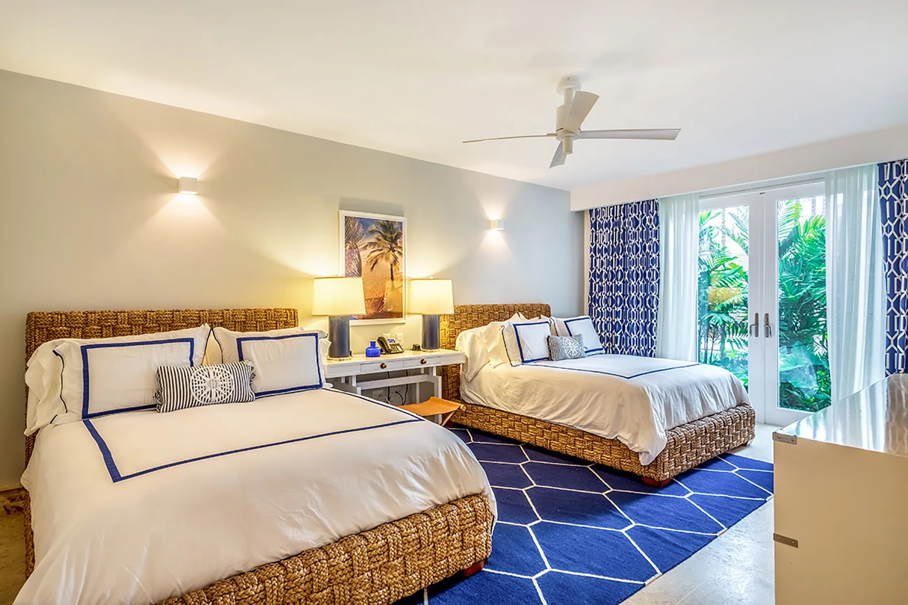Un dormitorio luminoso con dos camas, ropa de cama blanca y una alfombra azul estampada.