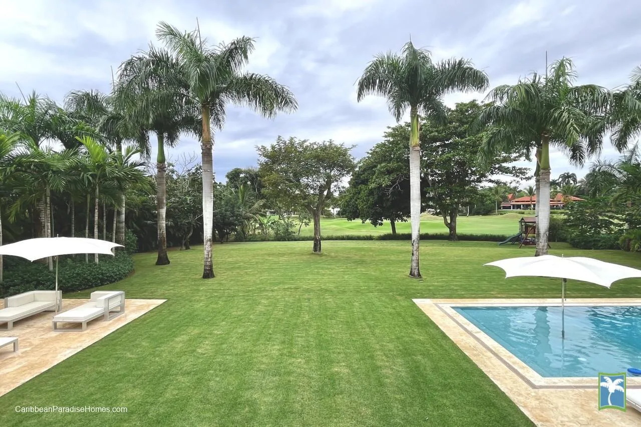 Un jardín con palmeras, asientos y una piscina.