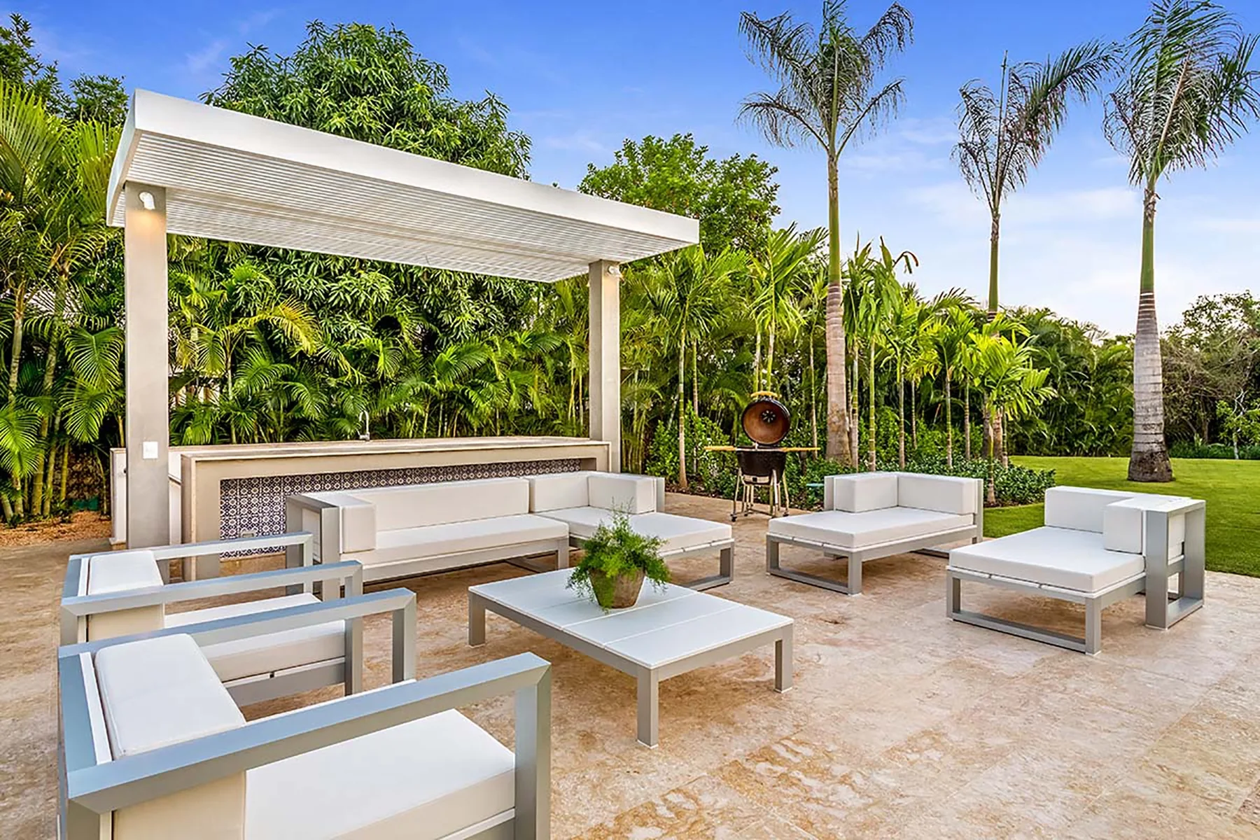 Un salón al aire libre con asientos acolchados y vegetación tropical.