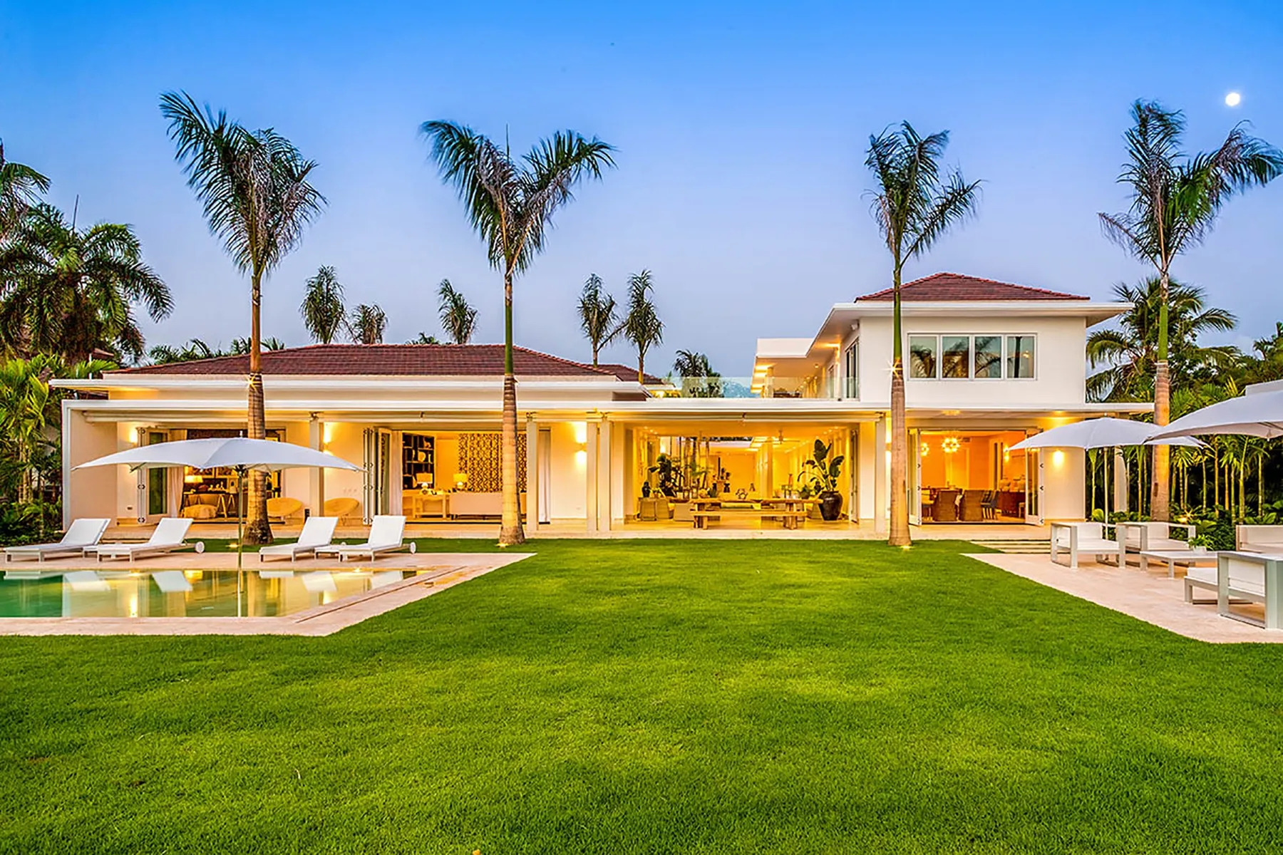 Una casa moderna con un amplio césped, palmeras y una piscina.