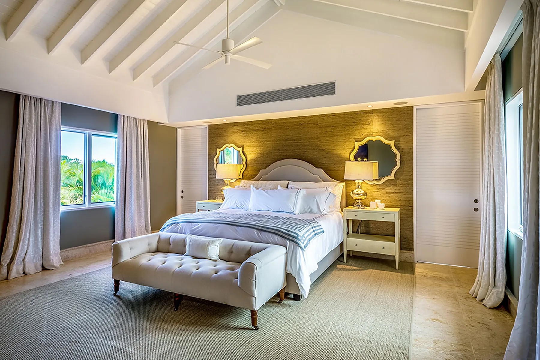 Un dormitorio con una cama, un banco acolchado y ventanas a ambos lados.