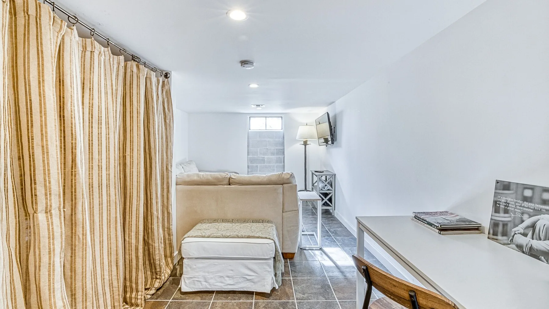 Una habitación luminosa con asientos beige, cortinas a rayas y un escritorio.