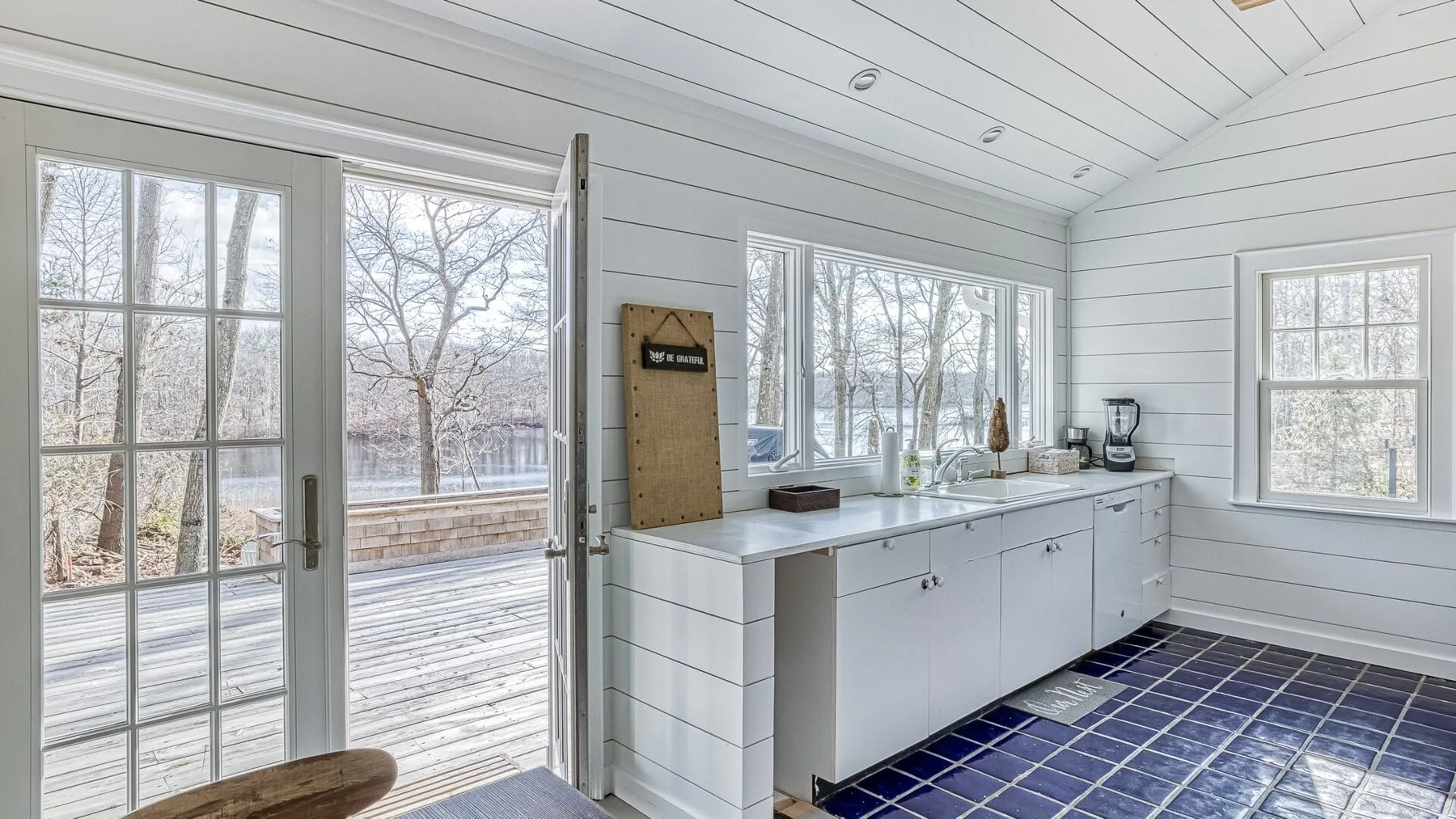 Una cocina luminosa con gabinetes blancos y grandes ventanas que dan a una terraza.