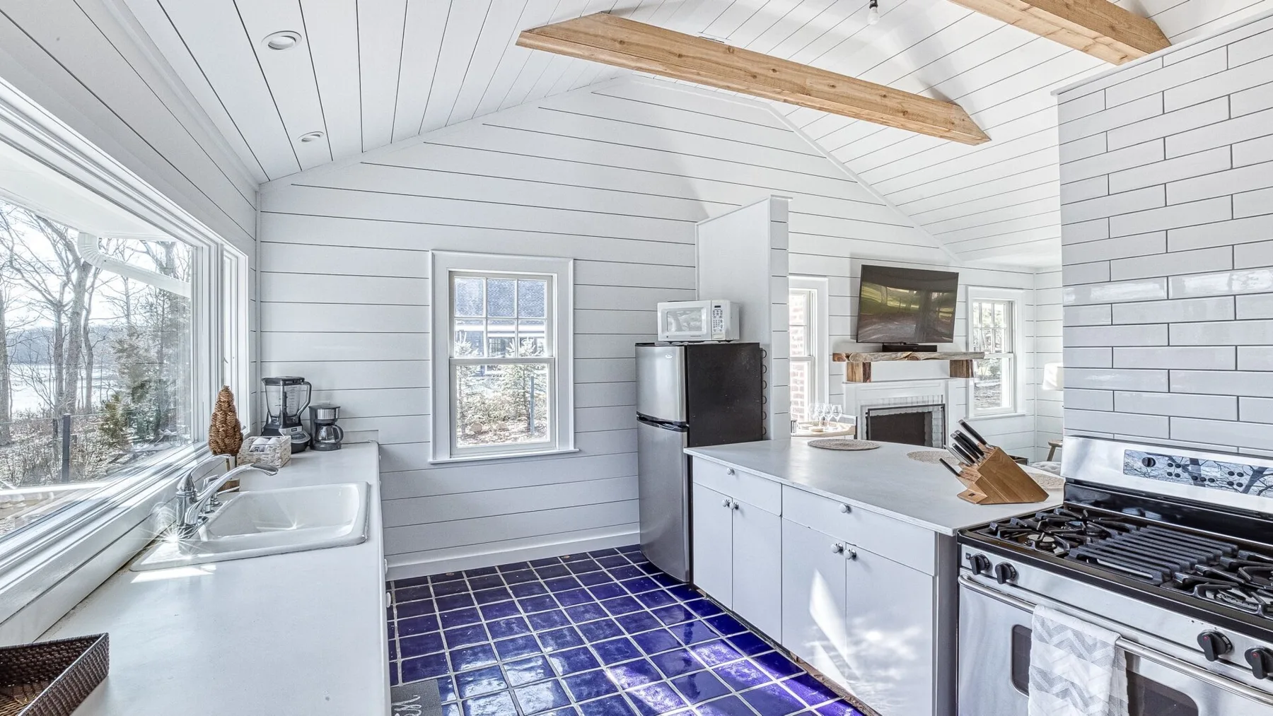 Una cocina luminosa con gabinetes blancos, una ventana grande y piso de baldosas.