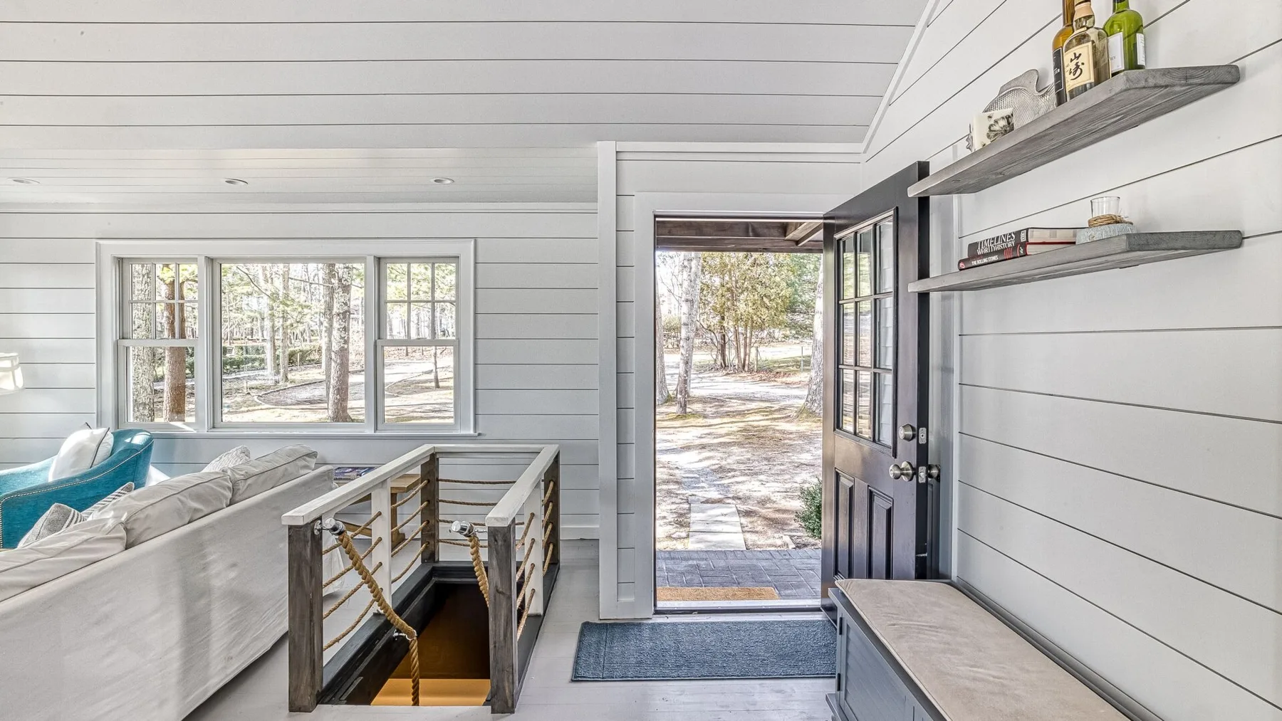 Una entrada luminosa con una puerta abierta, una escalera y ventanas con vista a los árboles.