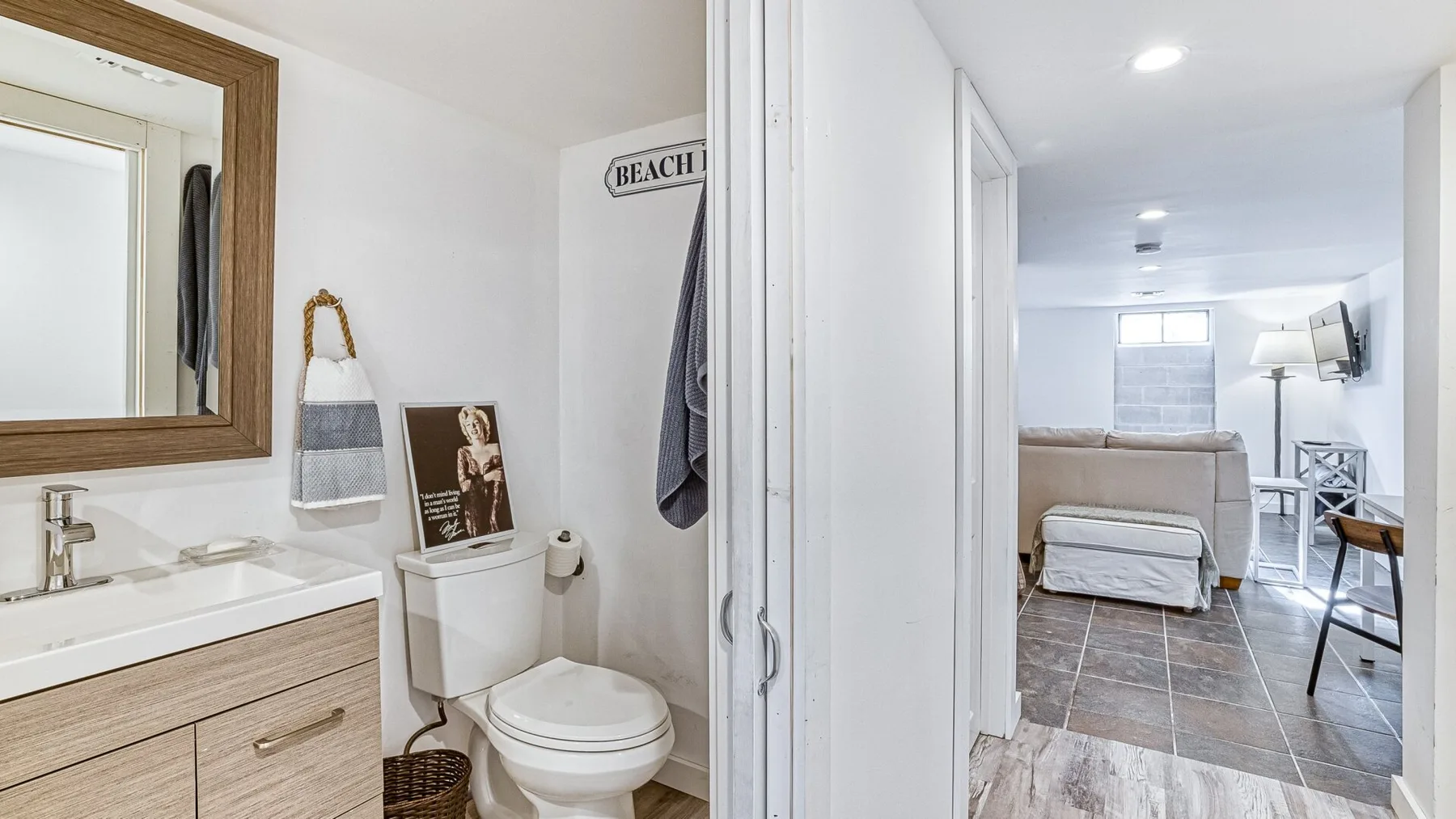 Un baño se abre a una habitación luminosa contigua con asientos y un televisor.