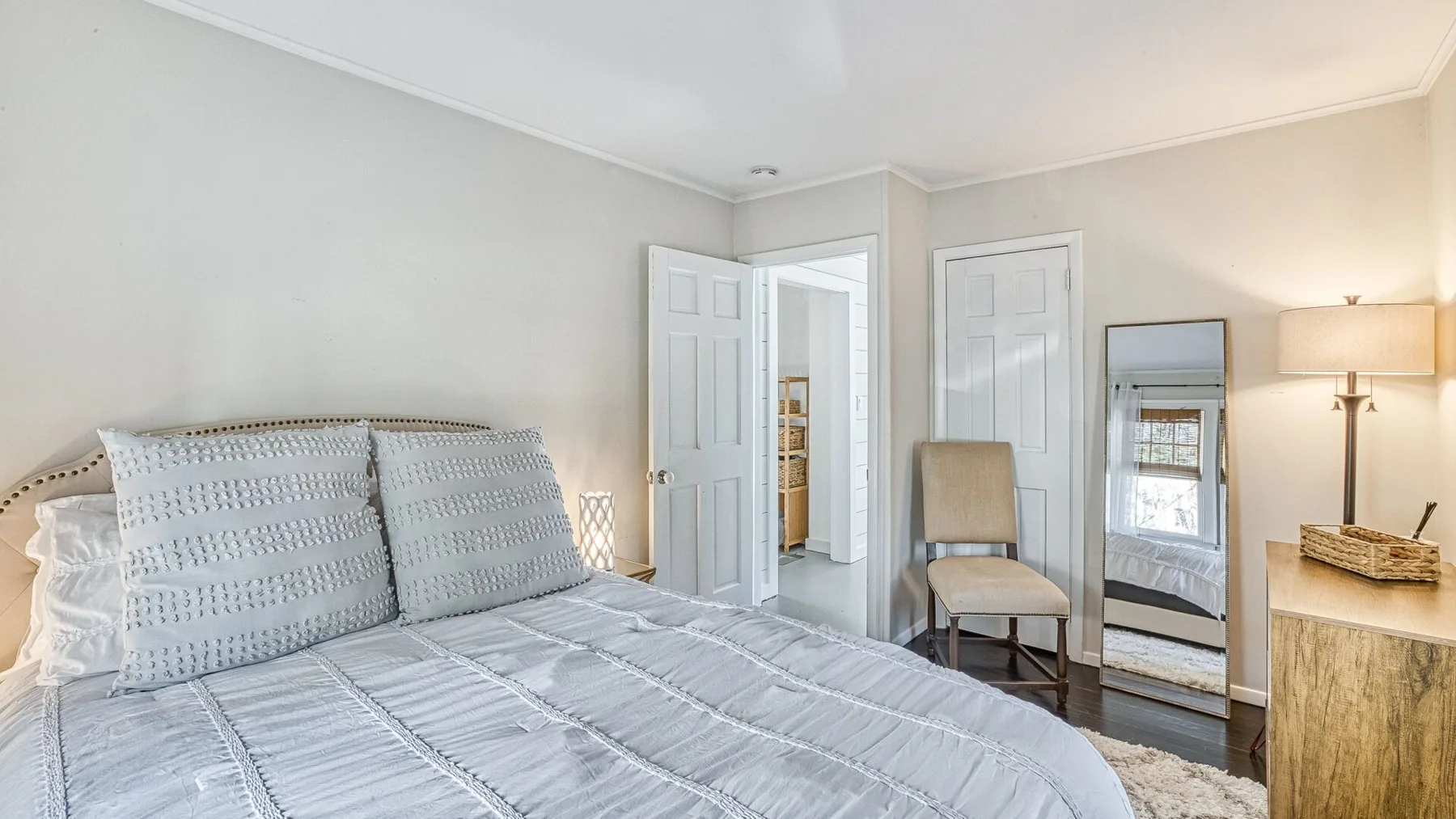 Un dormitorio luminoso con una cama, dos puertas y un espejo de cuerpo entero.