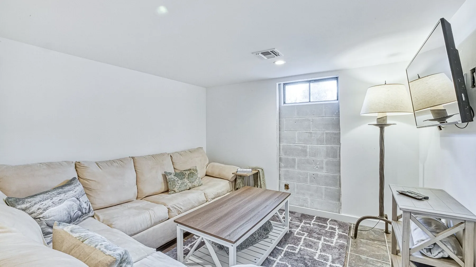 Una sala de estar con sofá seccional, mesa de centro y televisor montado en la pared.