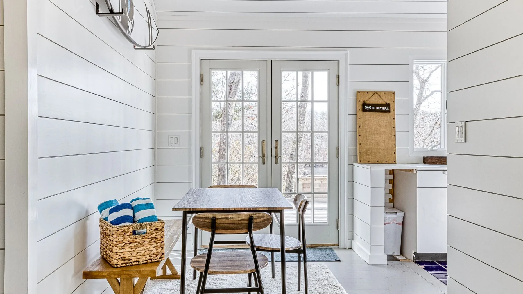 Un comedor luminoso con una mesa de madera junto a puertas de vidrio y una ventana.