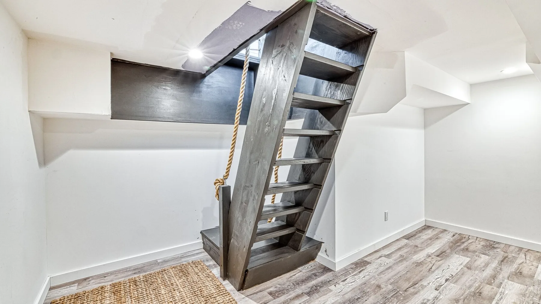 Una habitación interior luminosa tiene una escalera abierta y suelo claro con aspecto de madera.