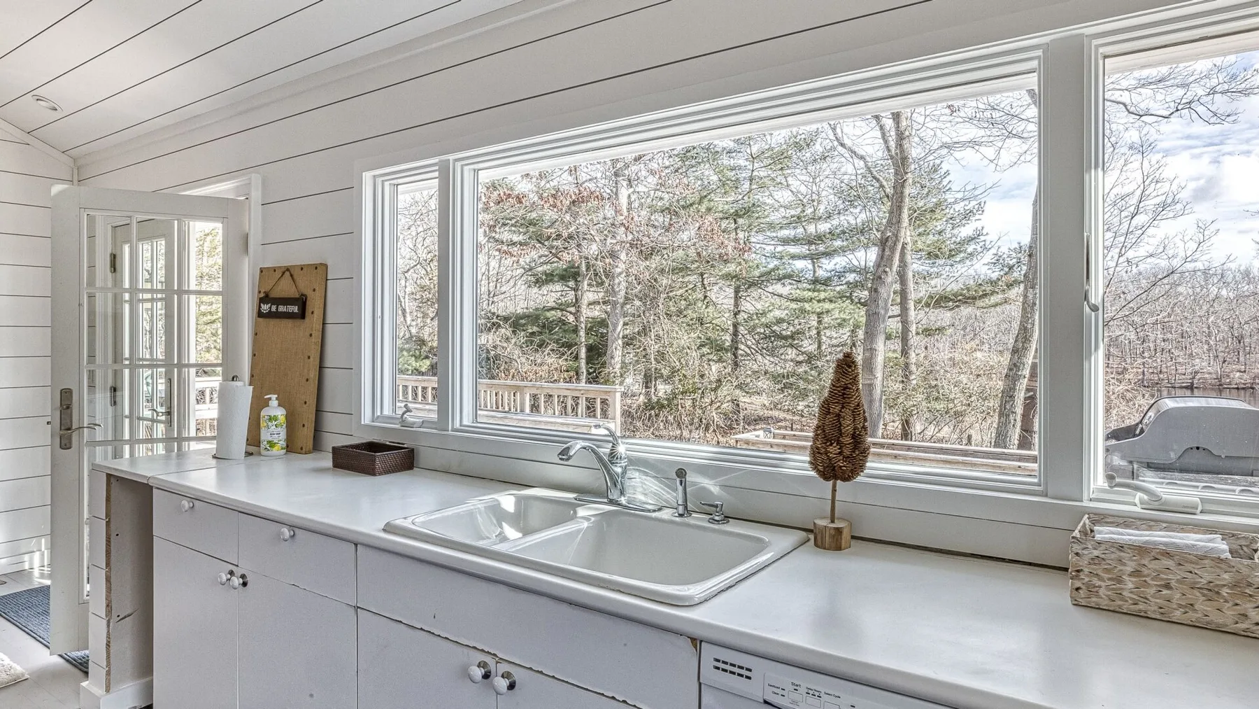 Una cocina luminosa con una encimera larga y grandes ventanas con vista a los árboles.