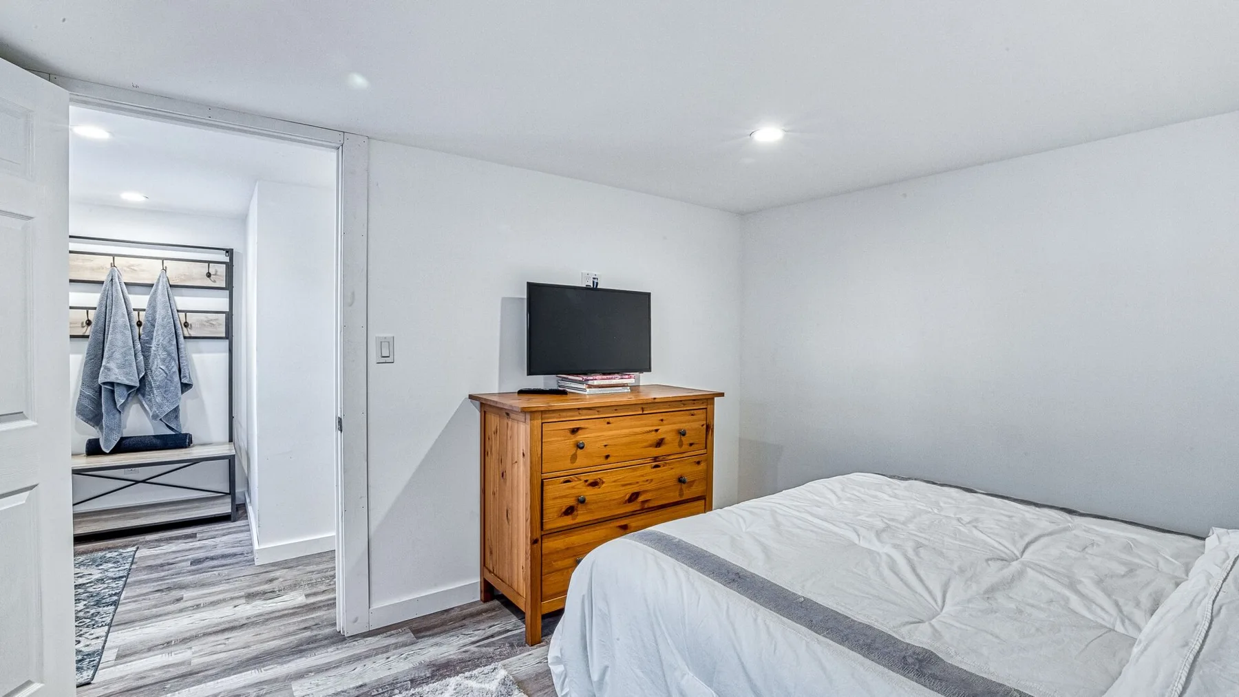 Un dormitorio con una cama y una cómoda de madera; una puerta abierta da a un armario.