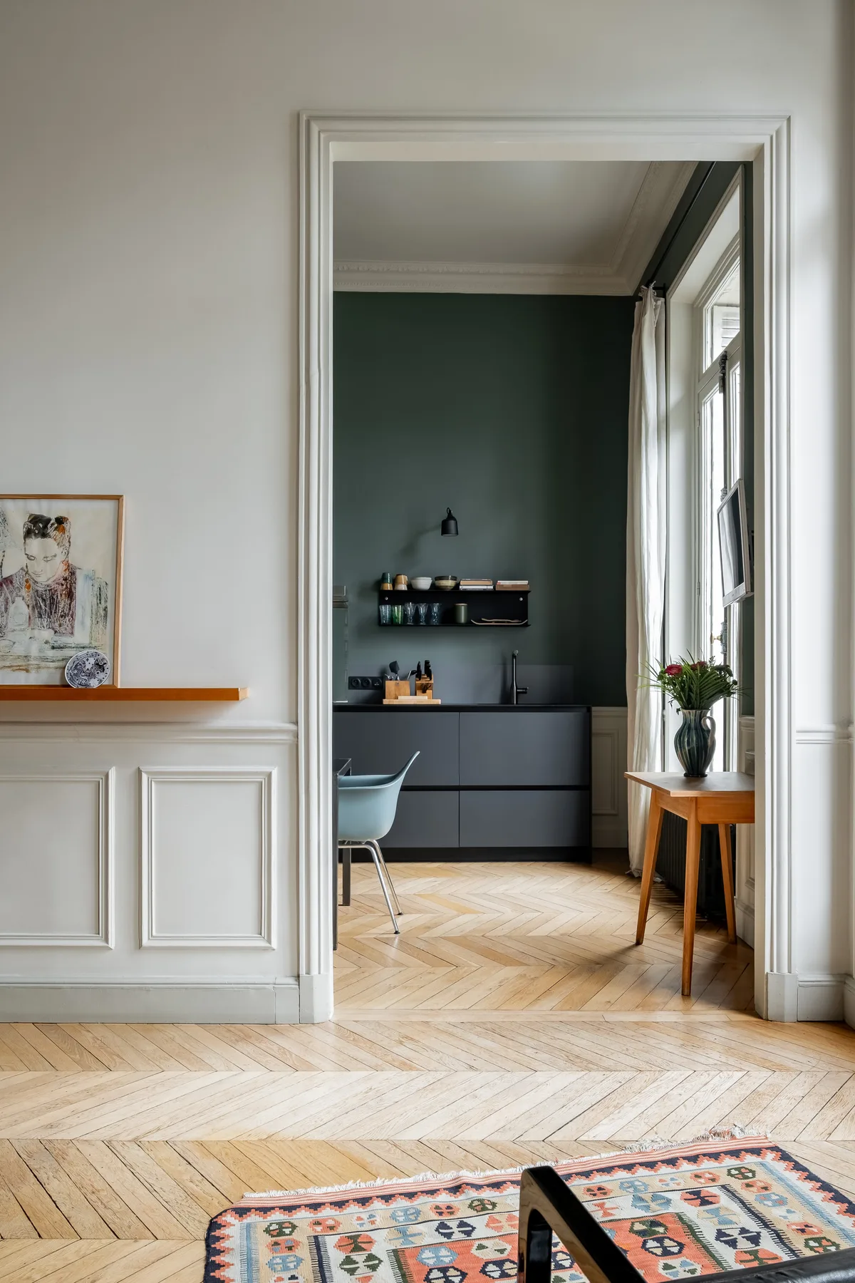 Una puerta da a una cocina de paredes oscuras con encimera y mesa.