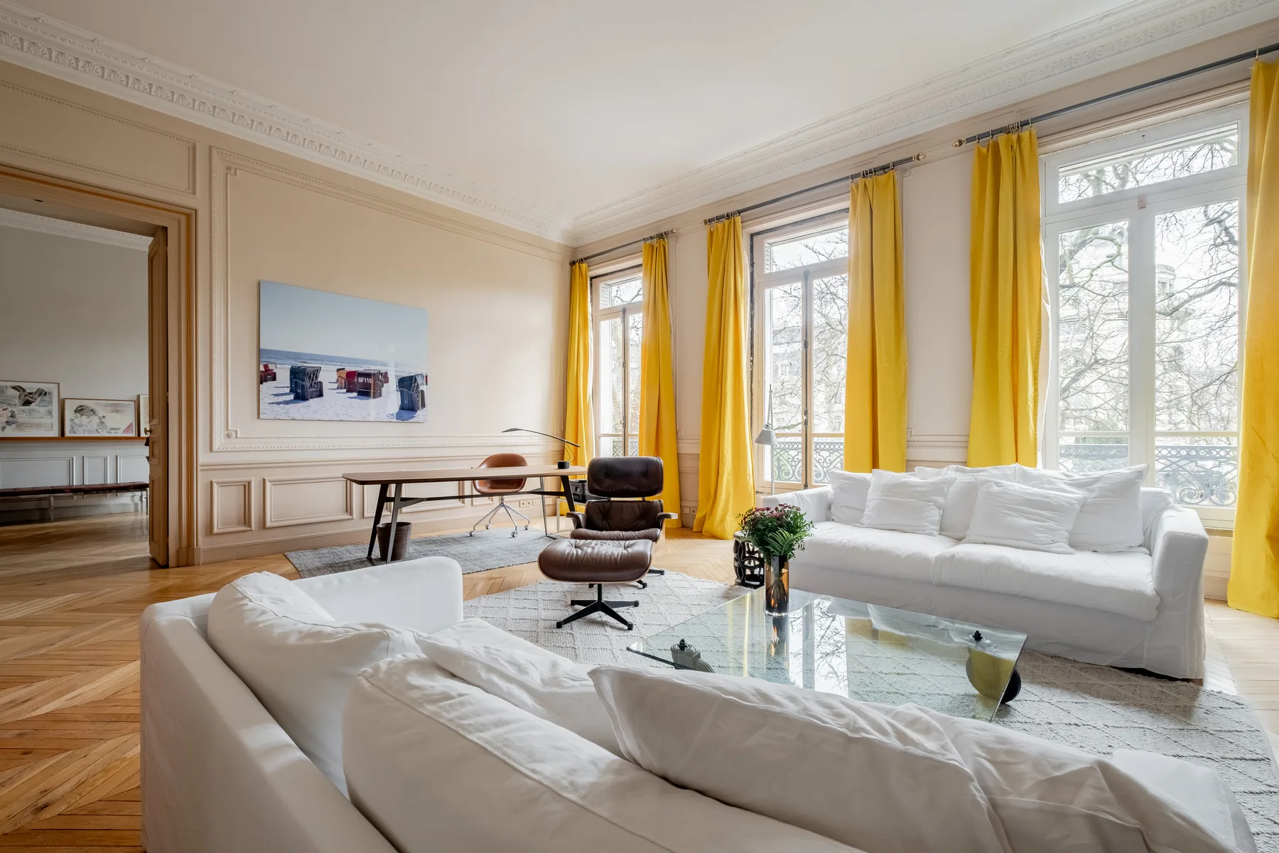 A bright living room with white seating, a glass coffee table, and yellow curtains.