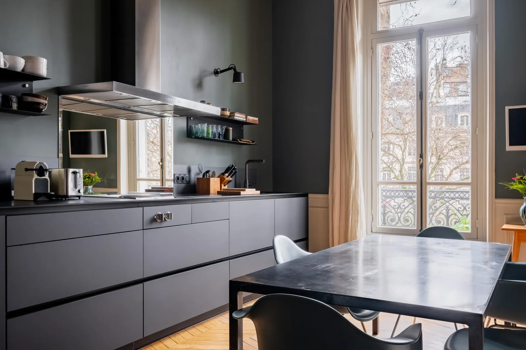 Una cocina y comedor modernos con gabinetes oscuros y ventanas altas.