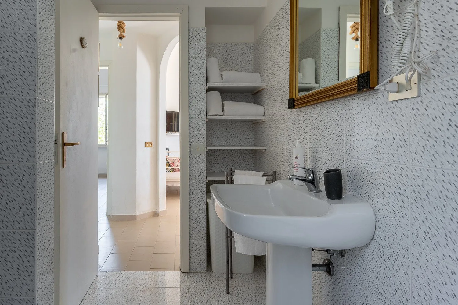 Un baño con lavabo y estantes abiertos junto a una puerta.