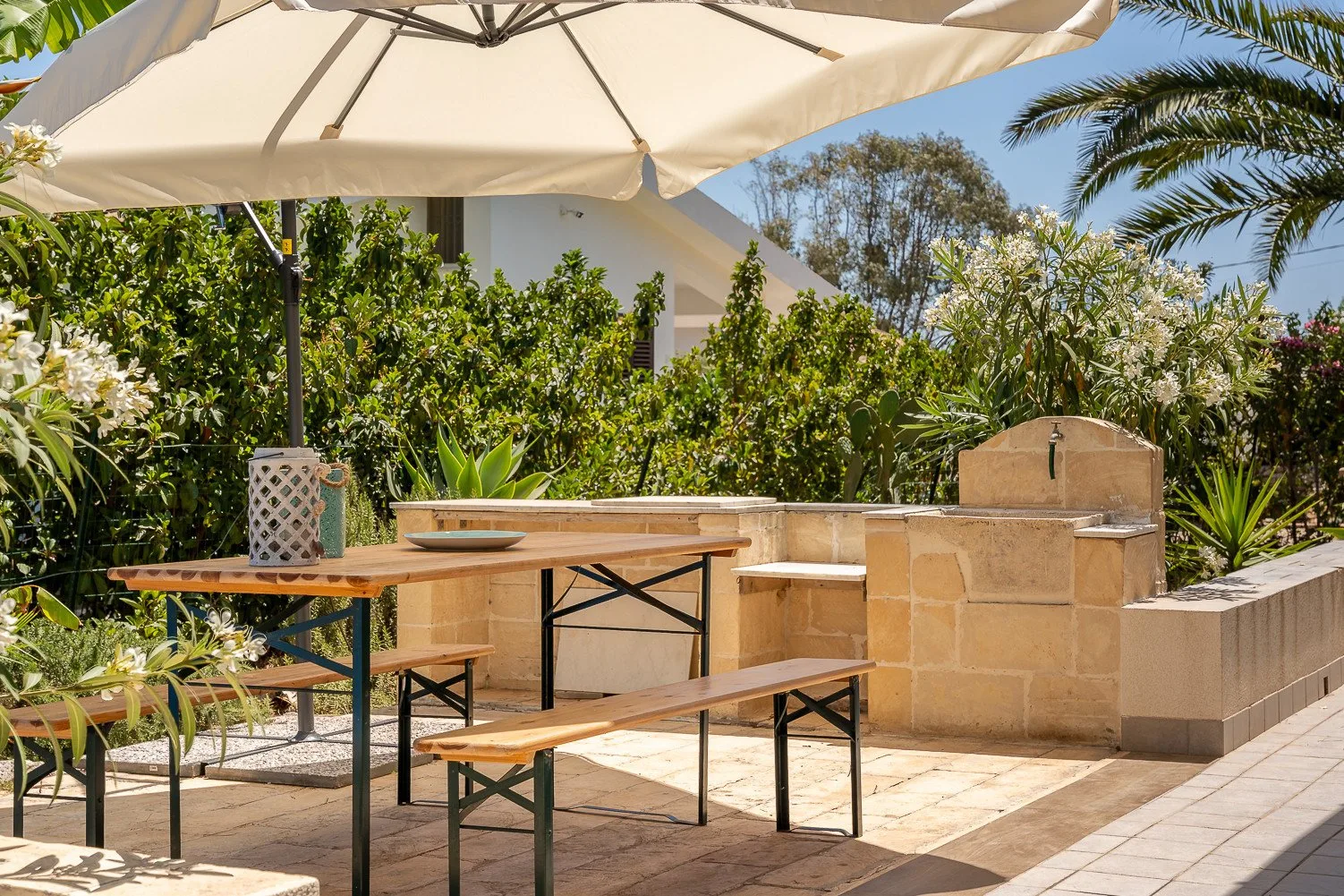 Un comedor al aire libre tiene una mesa de madera y bancos bajo una gran sombrilla.