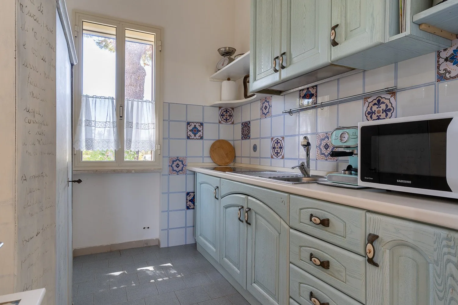 Una cocina compacta con gabinetes azul claro, azulejos decorados y una ventana.