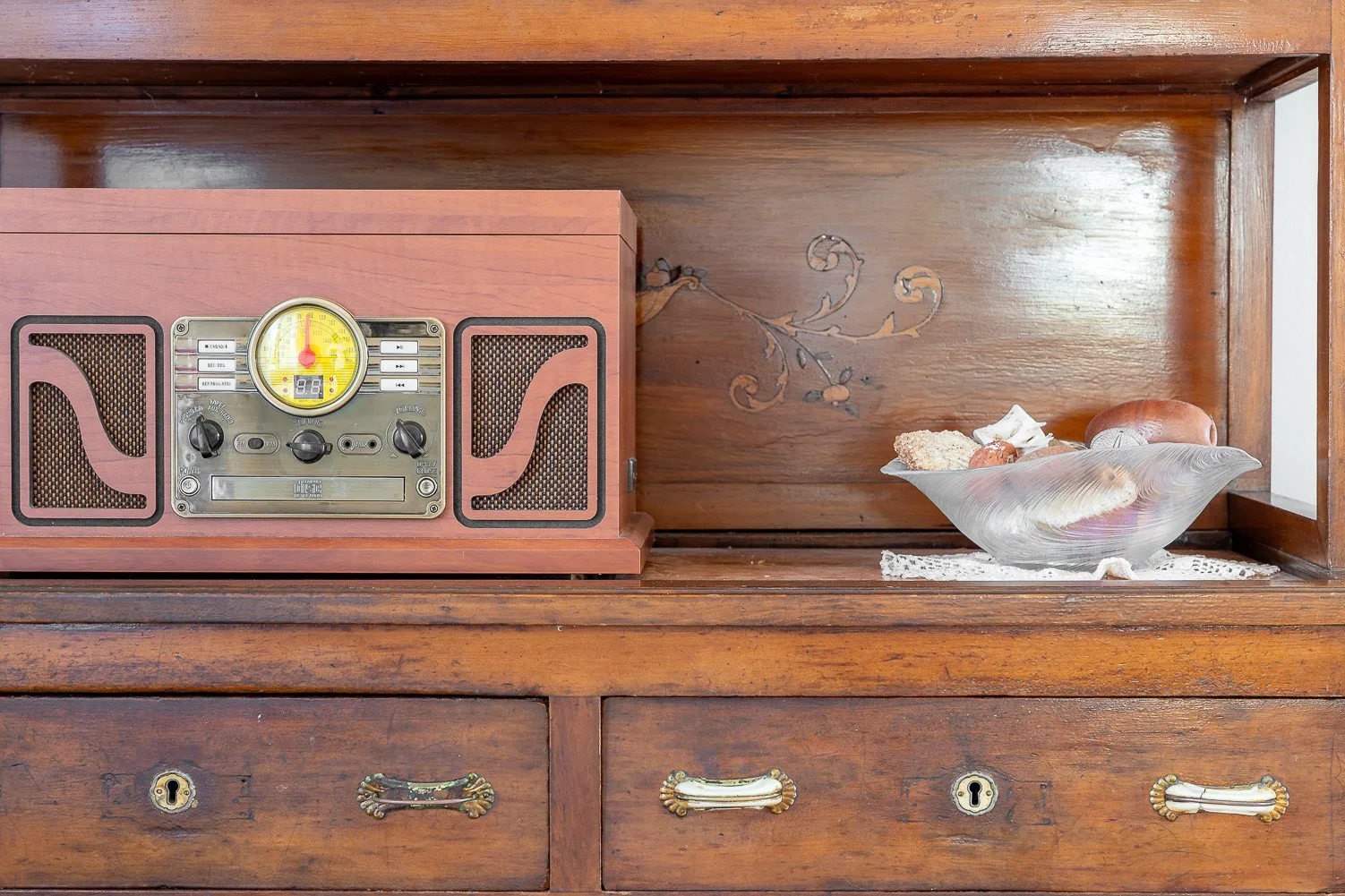 Un mueble de madera muestra una radio antigua junto a un cuenco decorativo.