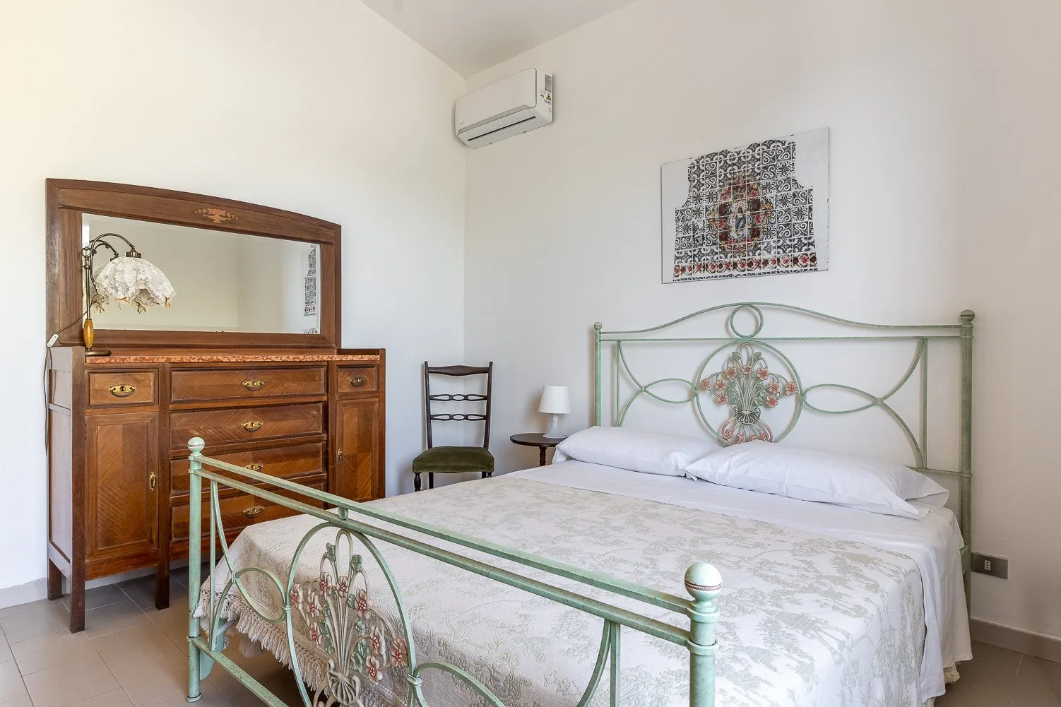 Un dormitorio con una cama de metal, una cómoda de madera y un aire acondicionado en la pared.