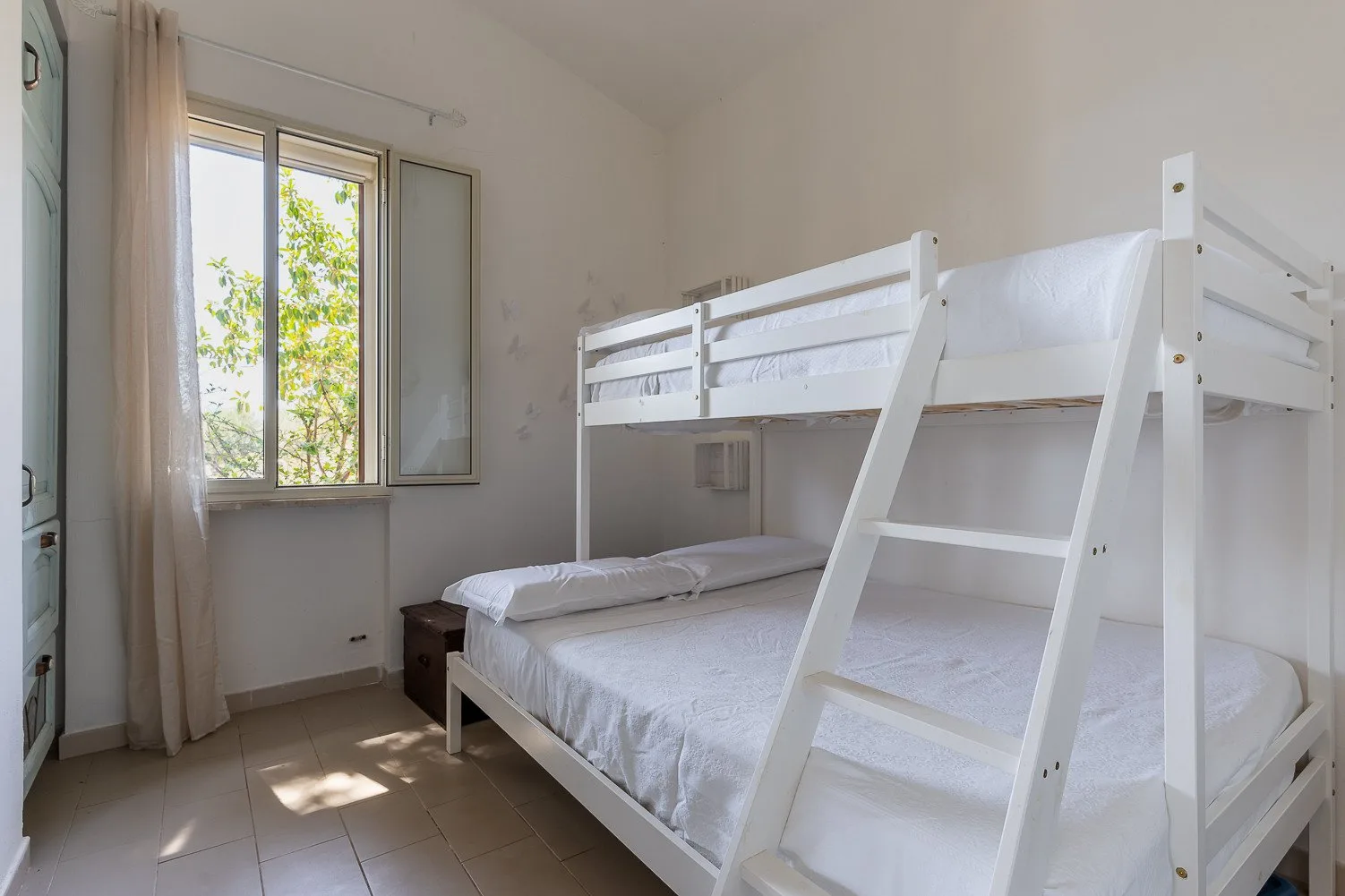 Un dormitorio luminoso con literas blancas y una ventana.