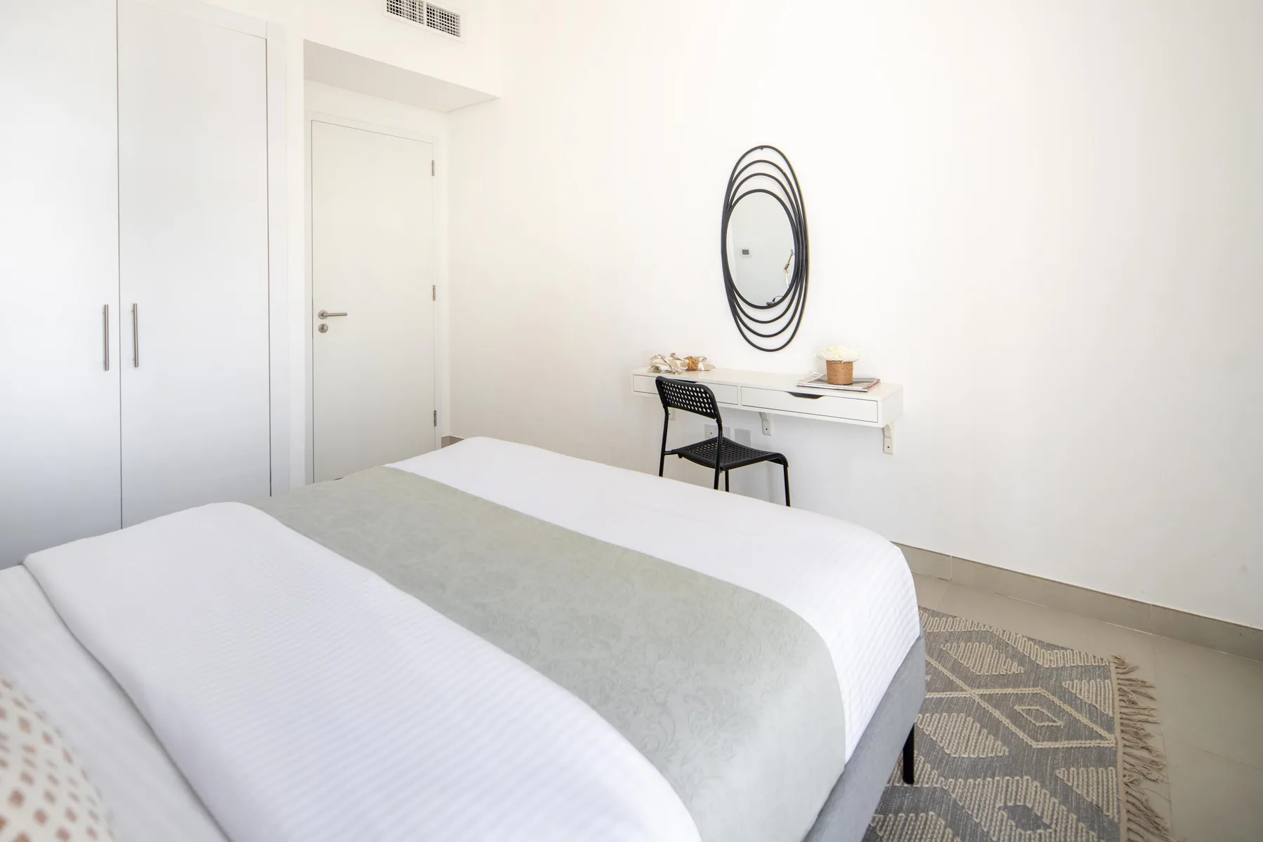 Un dormitorio luminoso con una cama bien hecha y un pequeño escritorio.