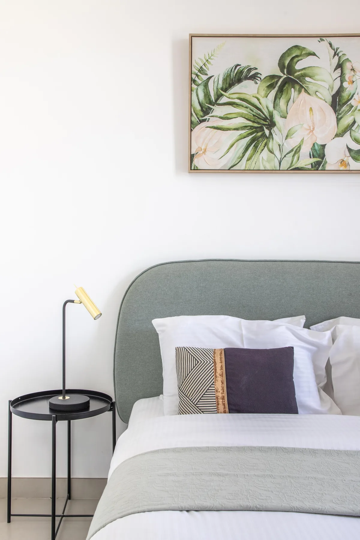 Dormitorio con cama, cabecero tapizado verde y arte botánico en la pared.
