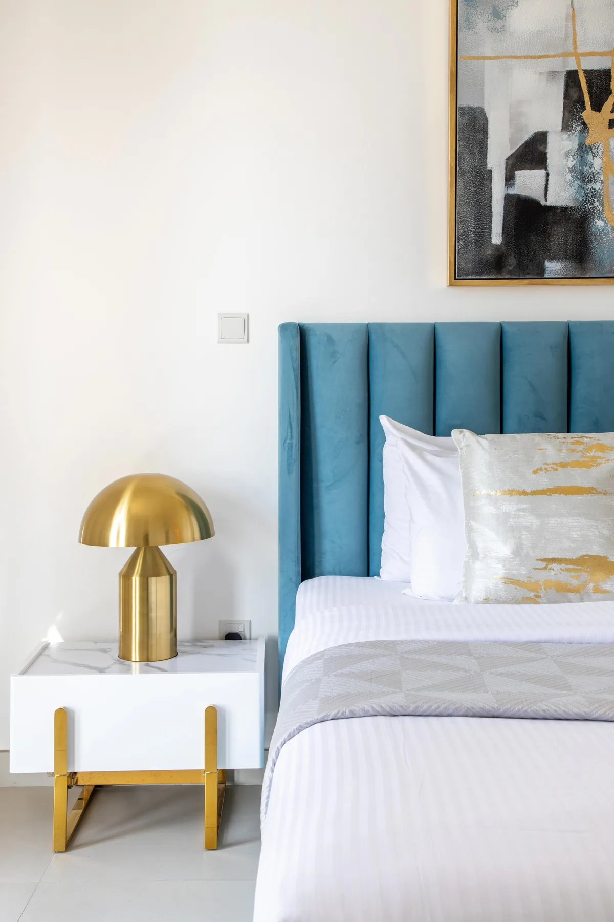 Dormitorio con cabecero tapizado en color turquesa, ropa de cama blanca y mesita de noche.